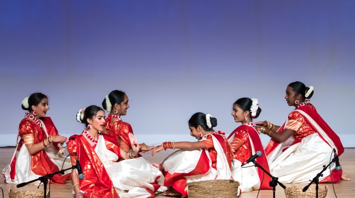 Women performing the Jhumur dance on stage with baskets.