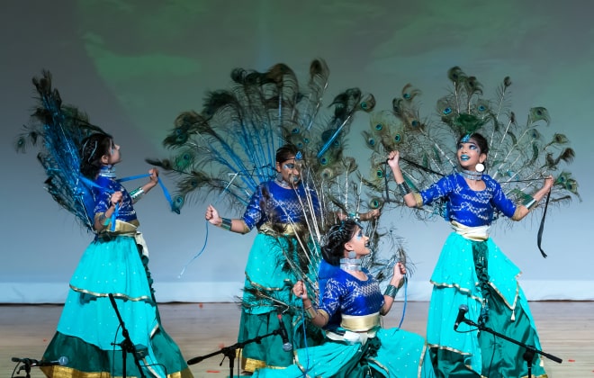 Students wearing peacock feather costumes and performing on stage.