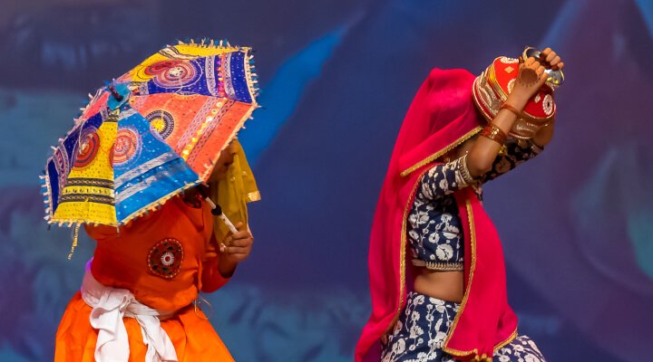 Students holding colorful umbrella and pots on stage.