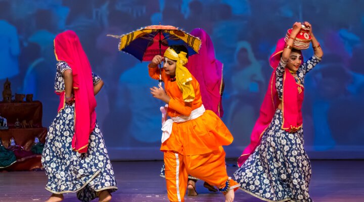 Young students wearing colorful outfits on stage.