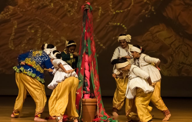 Dance performers circling around a pole tied with colorful cloth-based ropes.