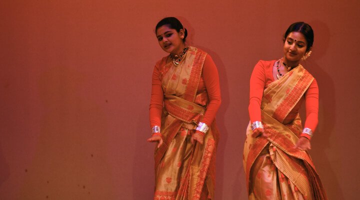 NSDA students in colorful attire performing Bihu on stage.
