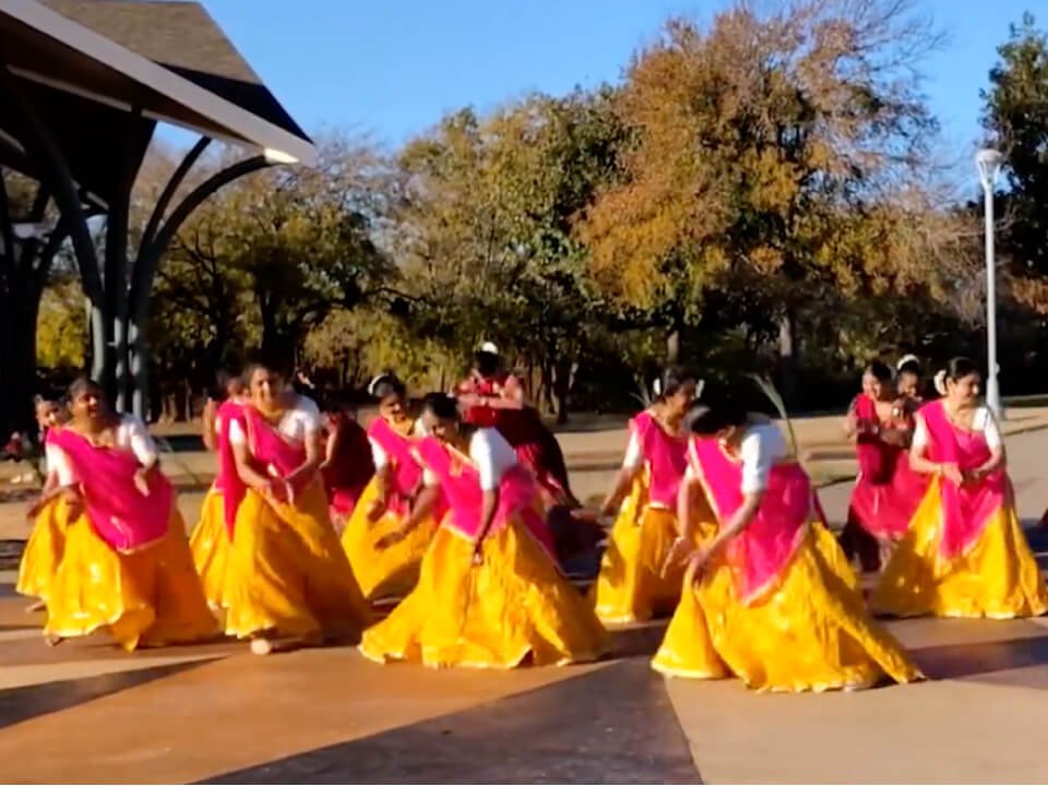 Women in colorful attire performing garba dance in the outdoors.