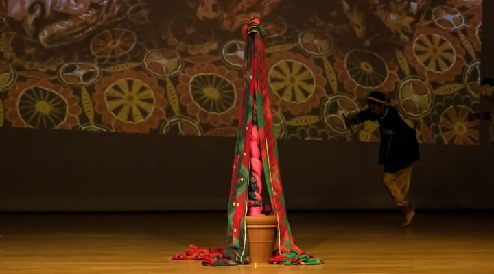 A pot with a vertical pole and wrapped with long pieces of colorful cloth.