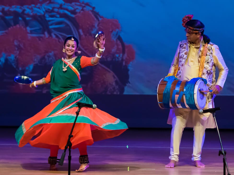 NSDA student dancing around a person playing the dhol (drum) live on stage.