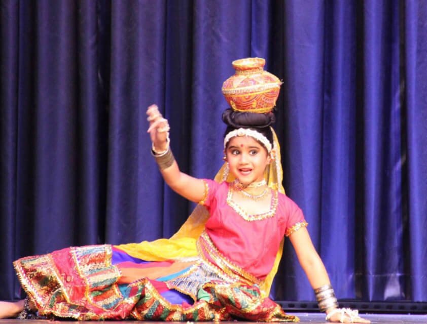 A young student performing an Indian folk dance, balancing a pot on her head.